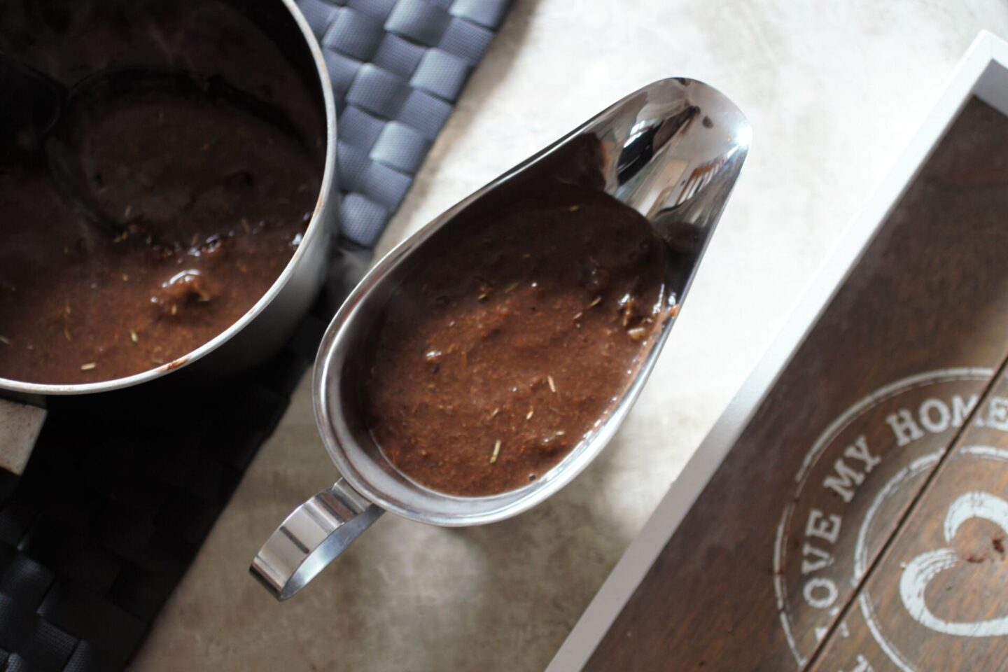 silver gravy jug filled with gravy, on a table next to a pan of prepared gravy.