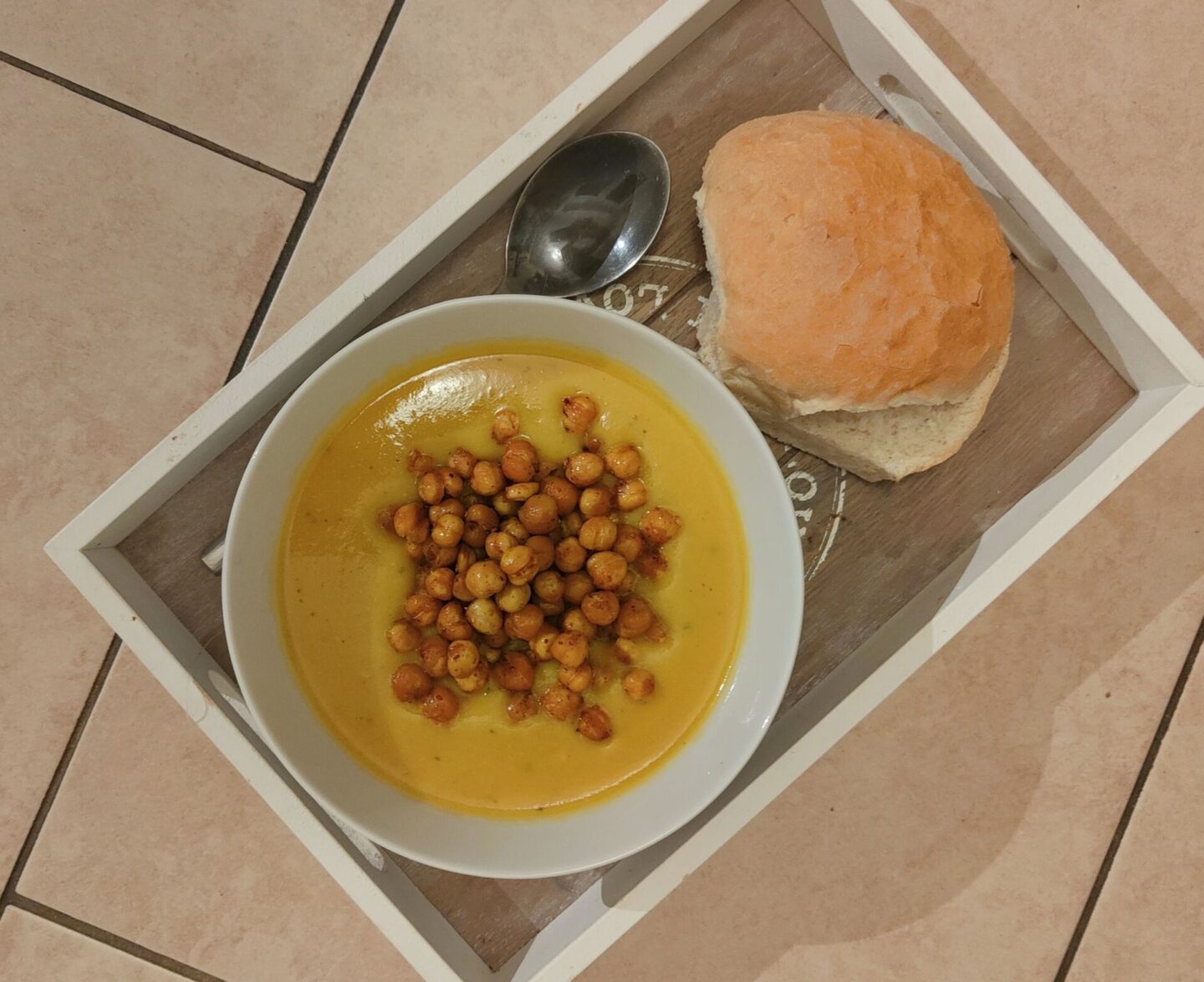 Bol soup in a white bowl, topped with roasted chickpeas. Both on a tray with a roll next to it