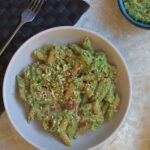 a bowl of broccoli & lime pesto pasta with a pot of broccoli & lime pesto placed next to it