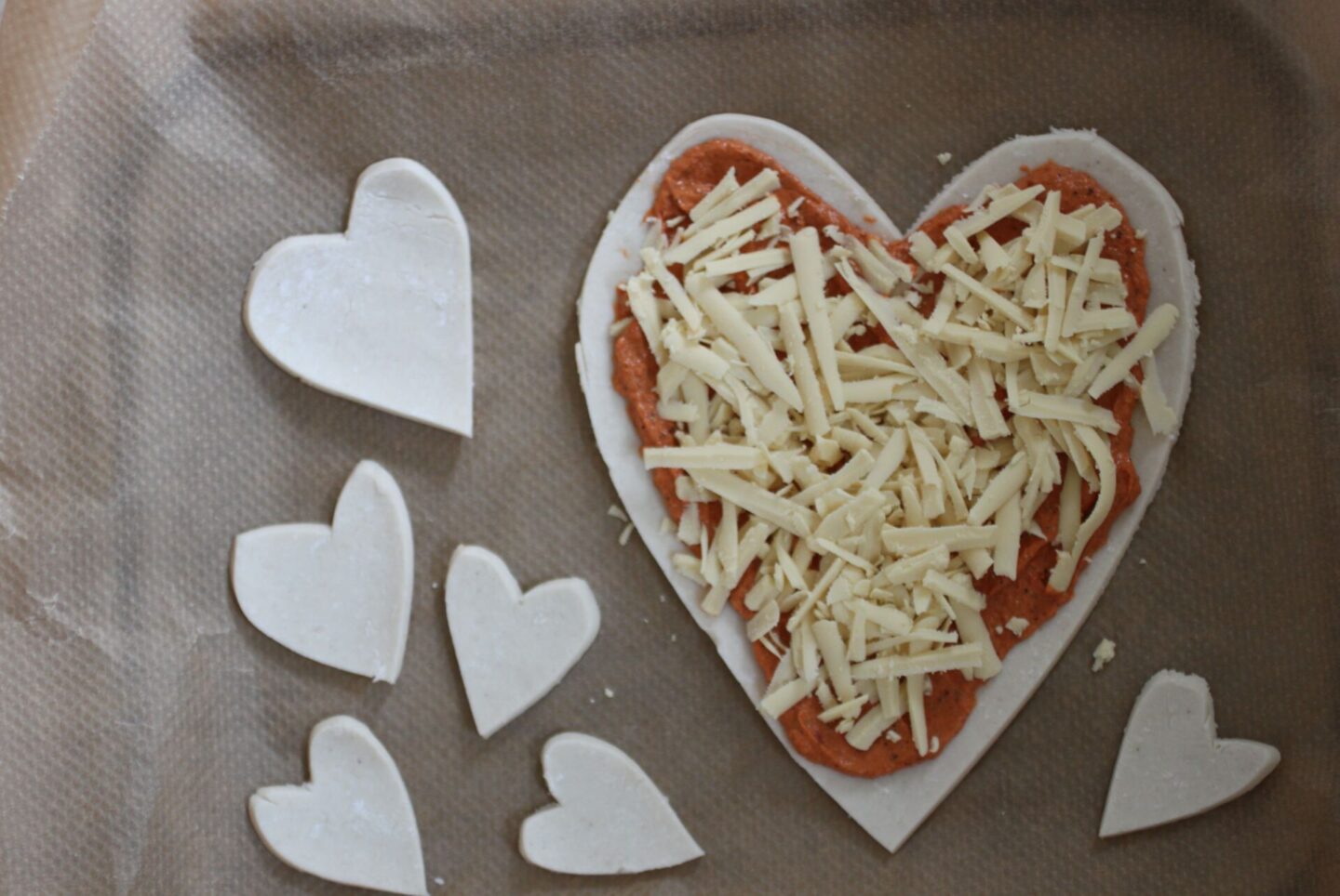 Pizza tart recipe and puff pastry hearts on a sheet of baking paper prior to being cooked