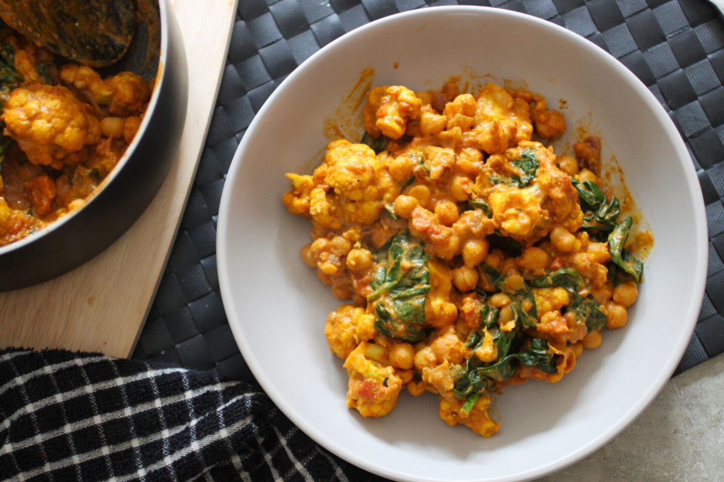 Bowl of cauliflower spinach curry on a table next to a pan of curry. 
