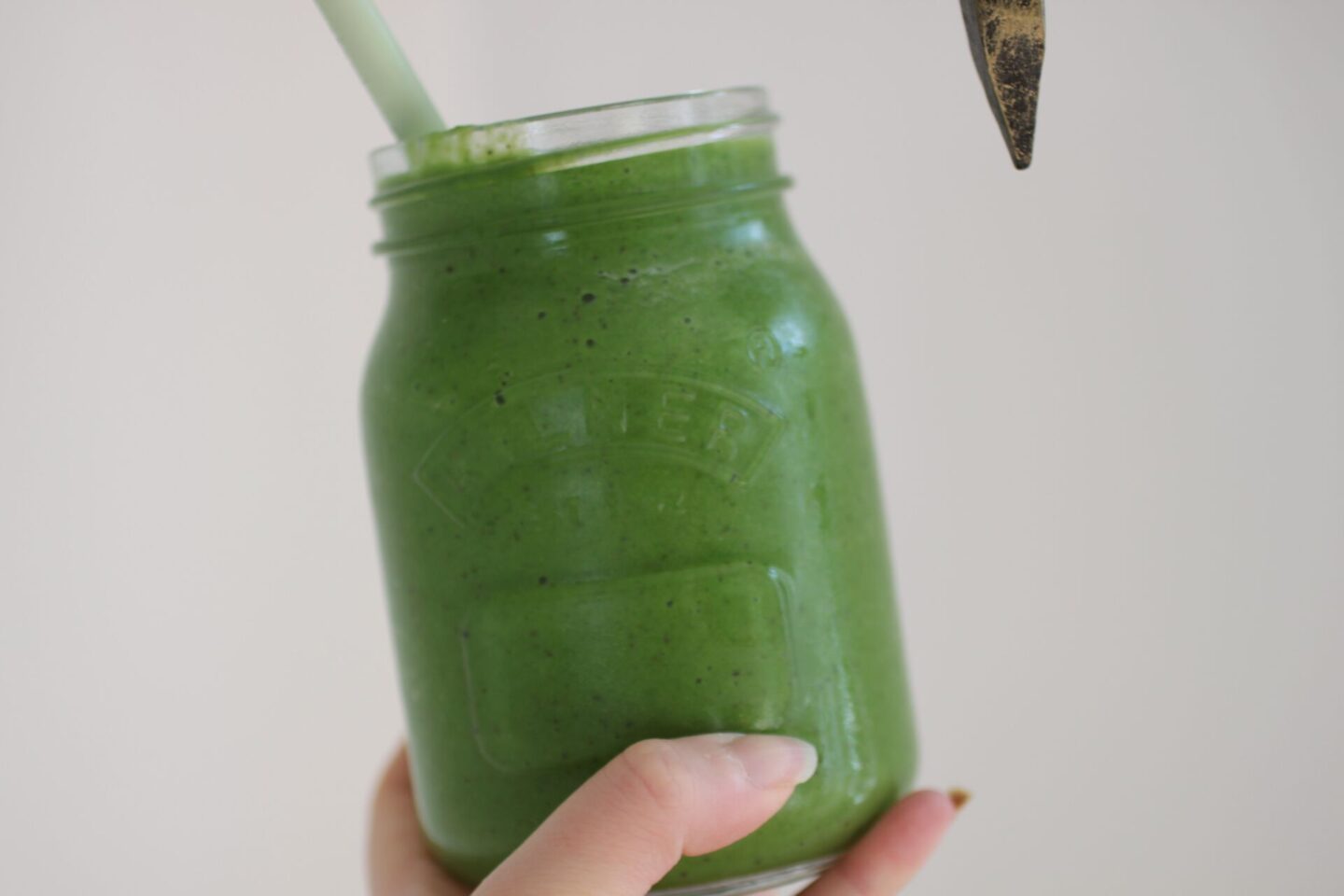 Sweet green smoothie recipe in a kilner jar, held against a white wall.