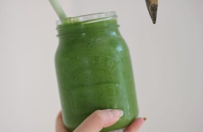 Sweet green smoothie recipe in a kilner jar, held against a white wall.