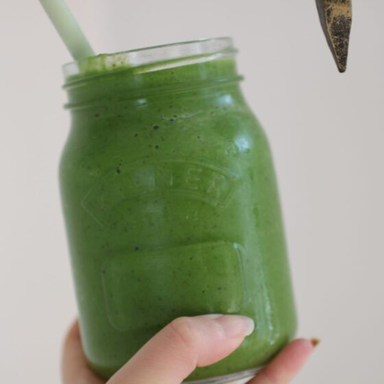 Sweet green smoothie recipe in a kilner jar, held against a white wall.