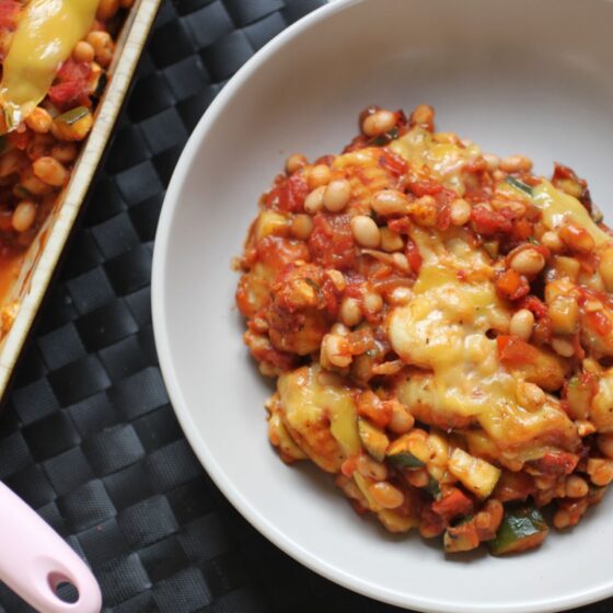 a bowl of baked gnocchi on a table, next to the baking dish filled with it