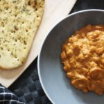bowl of butter chickpeas on a table, next to a free from naan bread