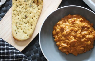 bowl of butter chickpeas on a table, next to a free from naan bread