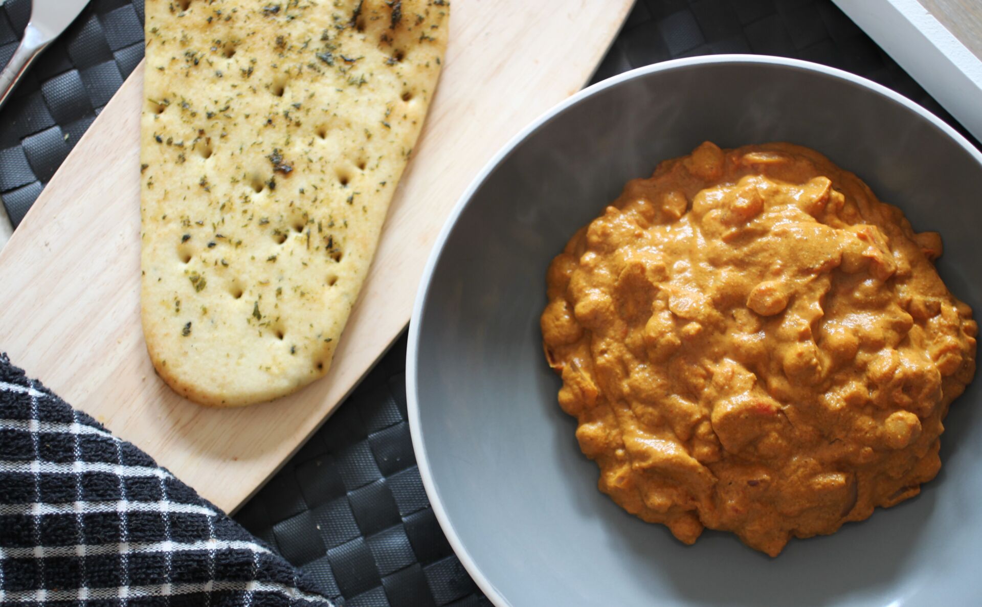 bowl of butter chickpeas on a table, next to a free from naan bread