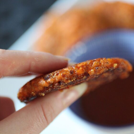a vegan carrot fritter held up to show the ideal thickness.
