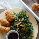 plate of cauliflower croquettes on a table, with a side salad and pot of barbecue sauce