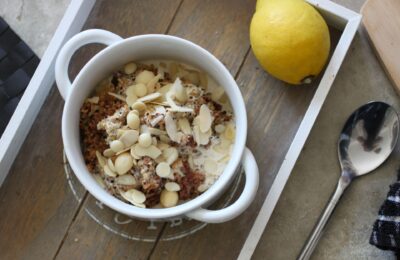 a bowl of lemon breakfast quinoa on a table, shot from above, placed next to a lemon and spoon
