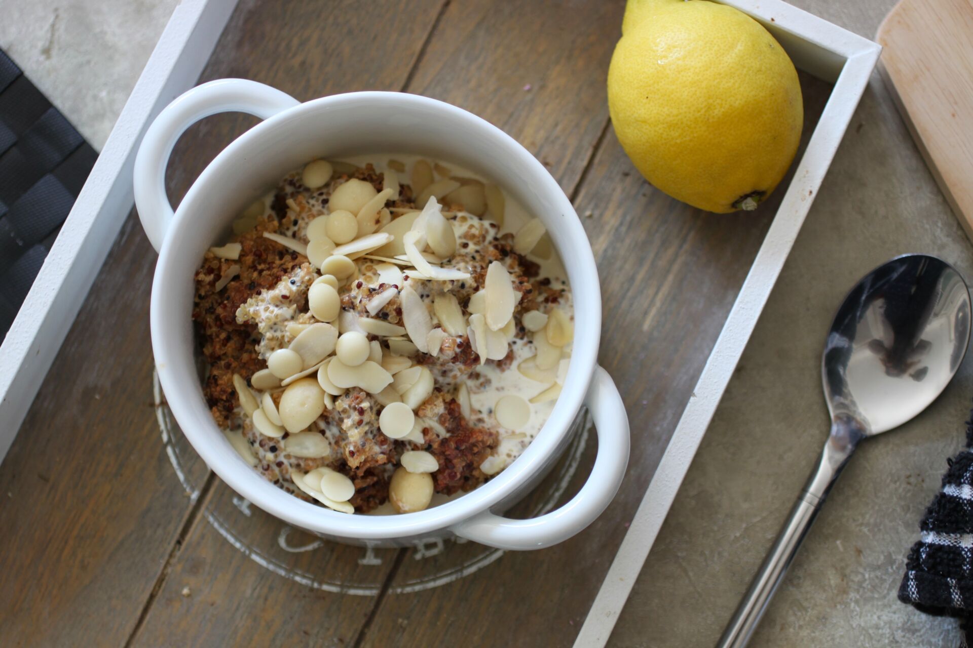 a bowl of lemon breakfast quinoa on a table, shot from above, placed next to a lemon and spoon