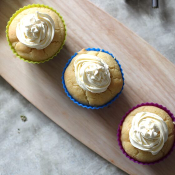 three lemon curd cupcakes on a wooden tray, shot from above.