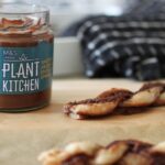 Jar of Plant Kitchen Chocolate Hazelnut Spread next to some vegan Nutella pastry twists on a sheet of greaseproof paper.