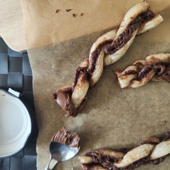 Vegan Nutella Pastry twists on a sheet of greaseproof paper with a spoon of nutella placed next to it