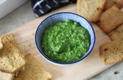 a pot of pea and rocket dip on a board with some crackers spread around it