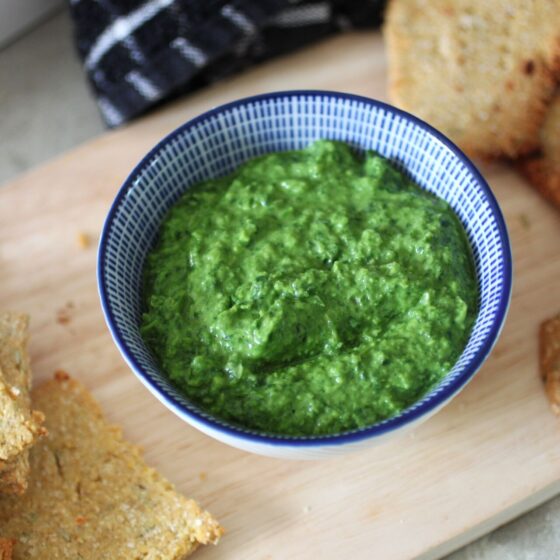 a pot of pea and rocket dip on a board with some crackers spread around it