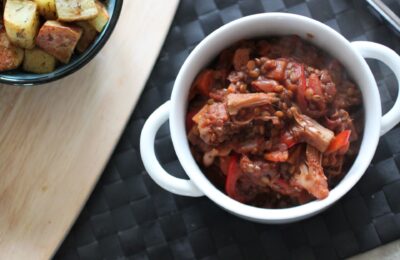 a bowl of jackfruit casserole on a black place mat with some potatoes in a dish to the side
