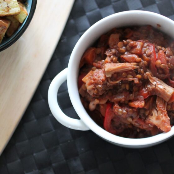 a bowl of jackfruit casserole on a black place mat with some potatoes in a dish to the side