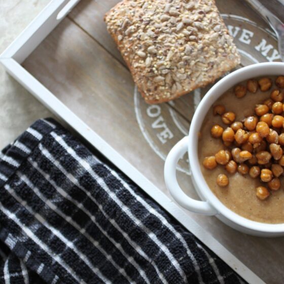 two bowls of spiced cauliflower soup on a dining table, one bowl placed on a tray with a bread roll