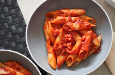 two large pasta bowls of vegan penne alla vodka on a dining table, shot from above
