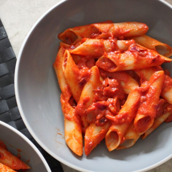 two large pasta bowls of vegan penne alla vodka on a dining table, shot from above