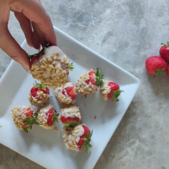 shot of white chocolate covered strawberries on a table with one being taken from the plate