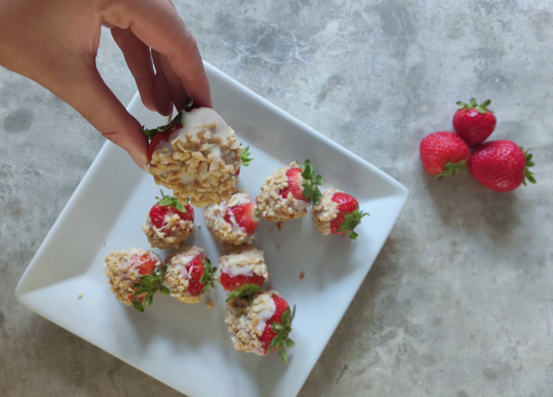 shot of white chocolate covered strawberries on a table with one being taken from the plate