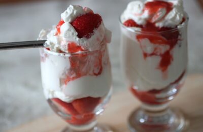 two glasses filled with Eton Mess with a spoon of Eton Mess resting on the top