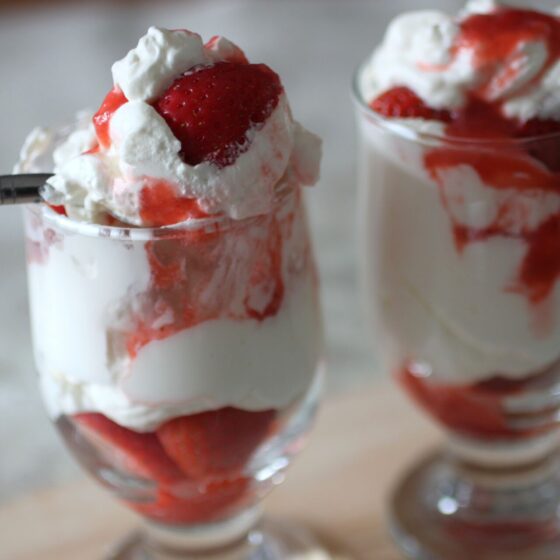 two glasses filled with Eton Mess with a spoon of Eton Mess resting on the top