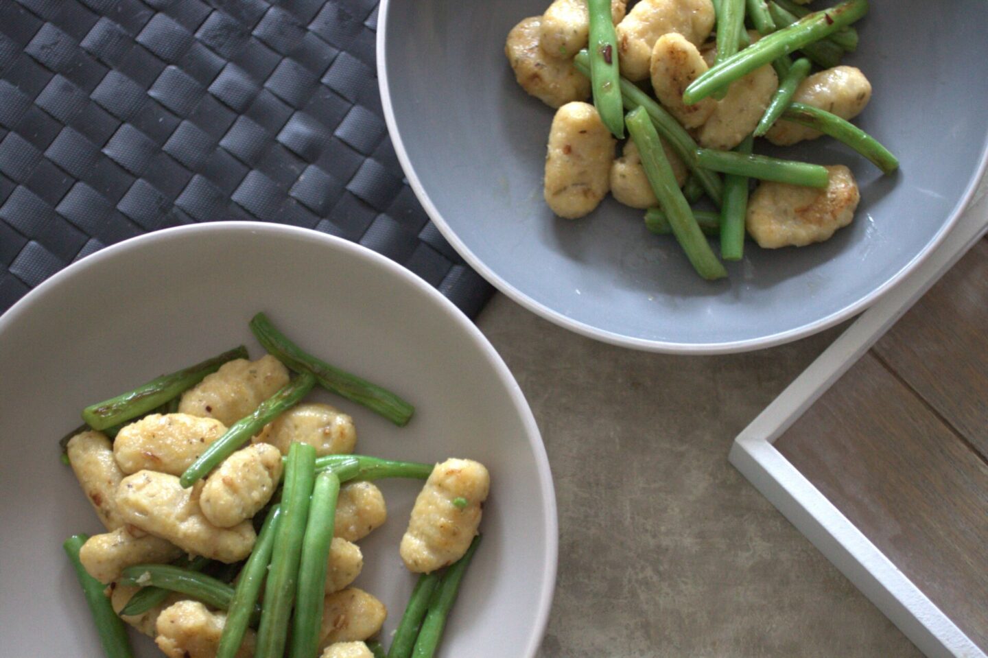 two bowls of gluten free vegan gnocchi with green beans, placed on a dining table