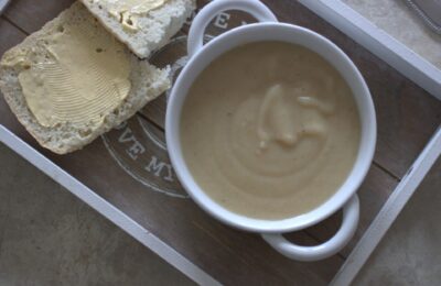 parsnip truffle soup in a white bowl placed on a grey tray with a gluten free ciabatta