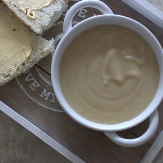 parsnip truffle soup in a white bowl placed on a grey tray with a gluten free ciabatta