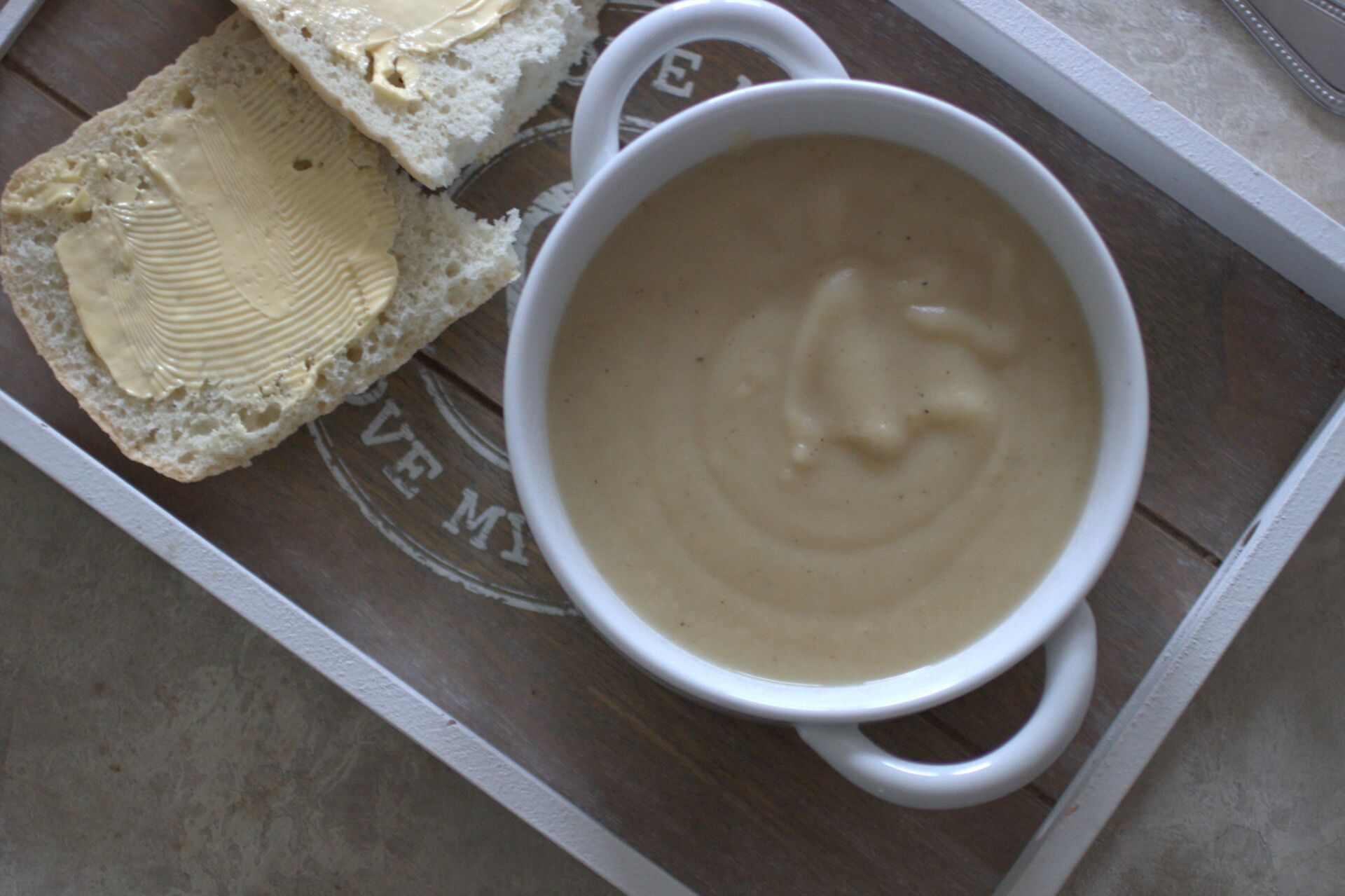 parsnip truffle soup in a white bowl placed on a grey tray with a gluten free ciabatta