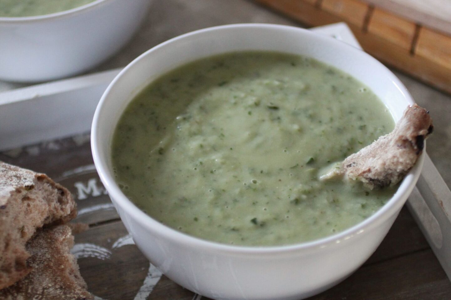 a bowl of kale & celeriac soup on a wooden board with bread