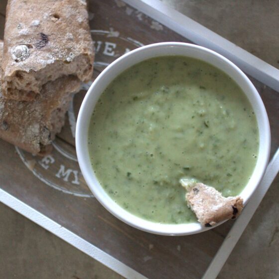 a bowl of kale & celeriac soup on a wooden board with an olive baguette