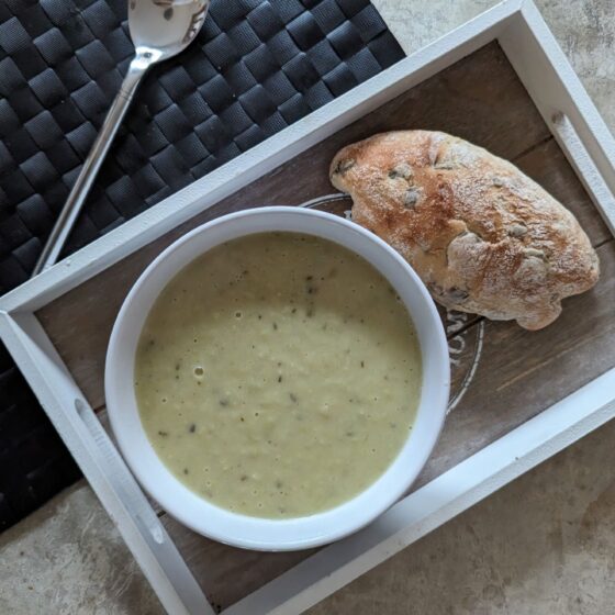 bowl of leek soup recipe on a tray next to a bread roll