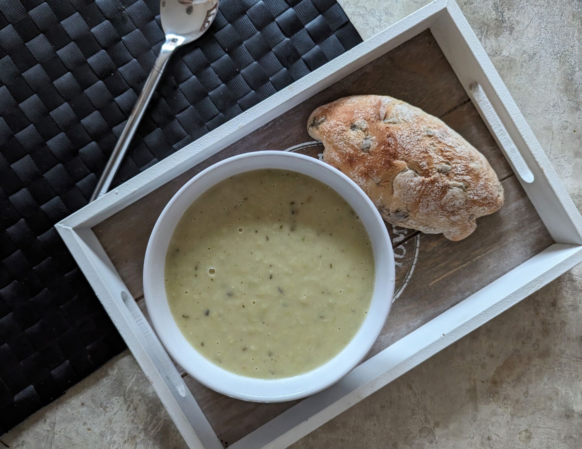 bowl of leek soup recipe on a tray next to a bread roll