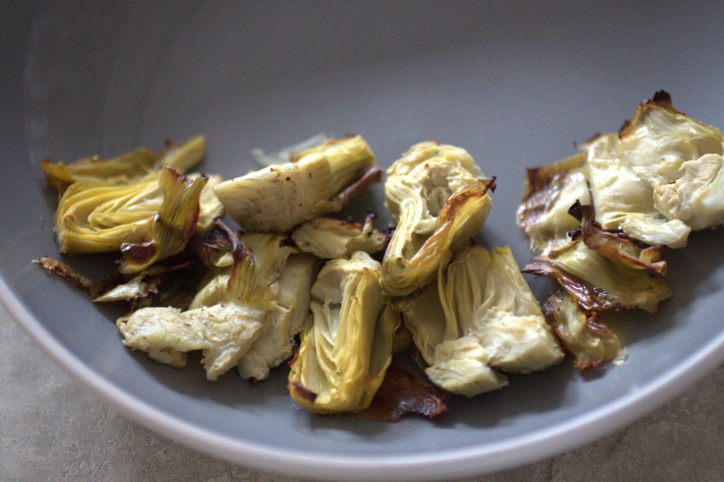 close up shot of roasted artichoke hearts in grey bowl