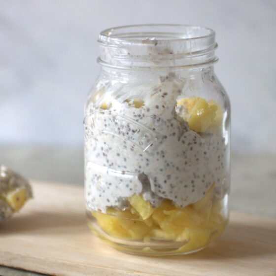 creamy pineapple breakfast pot in a Kilner jar placed on a wooden tray with a spoon with the creamy oats placed on a tray