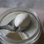 a pot of vegan lemon mousse with a spoon of lemon mousse placed on top to show the whipped texture of the mousse