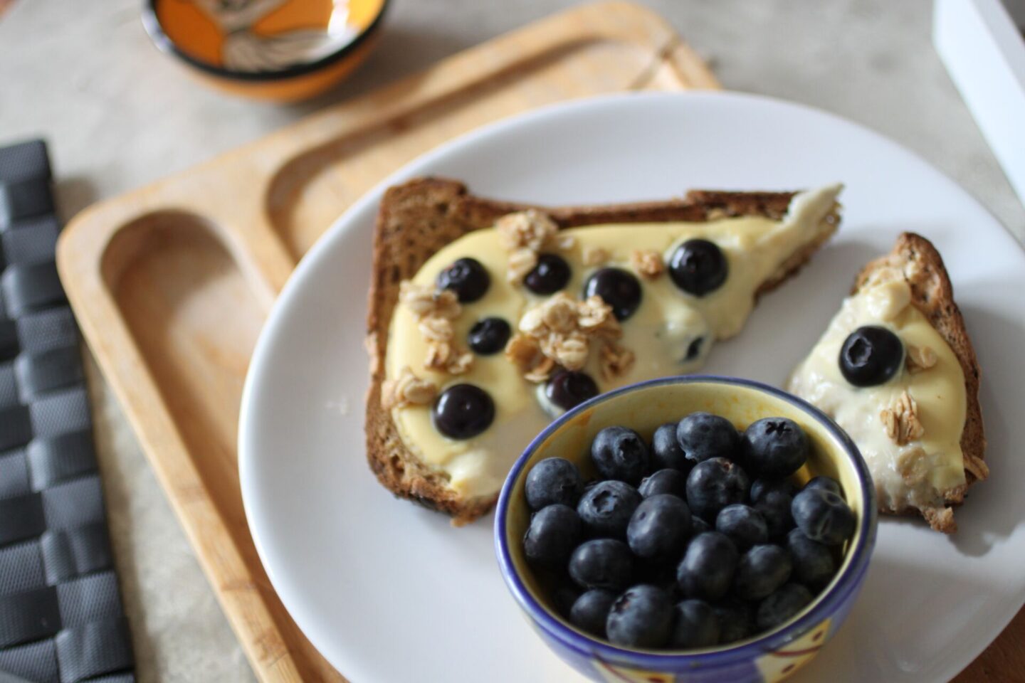 plate of yoghurt toast with blueberries with a close up of a pot of blueberries to the side