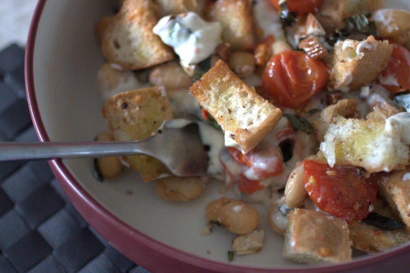 a close up shot of a bowl of butter bean bruschetta bake with a fork in