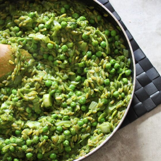 a pan of freshly cooked orzo risotto with a wooden spoon in it