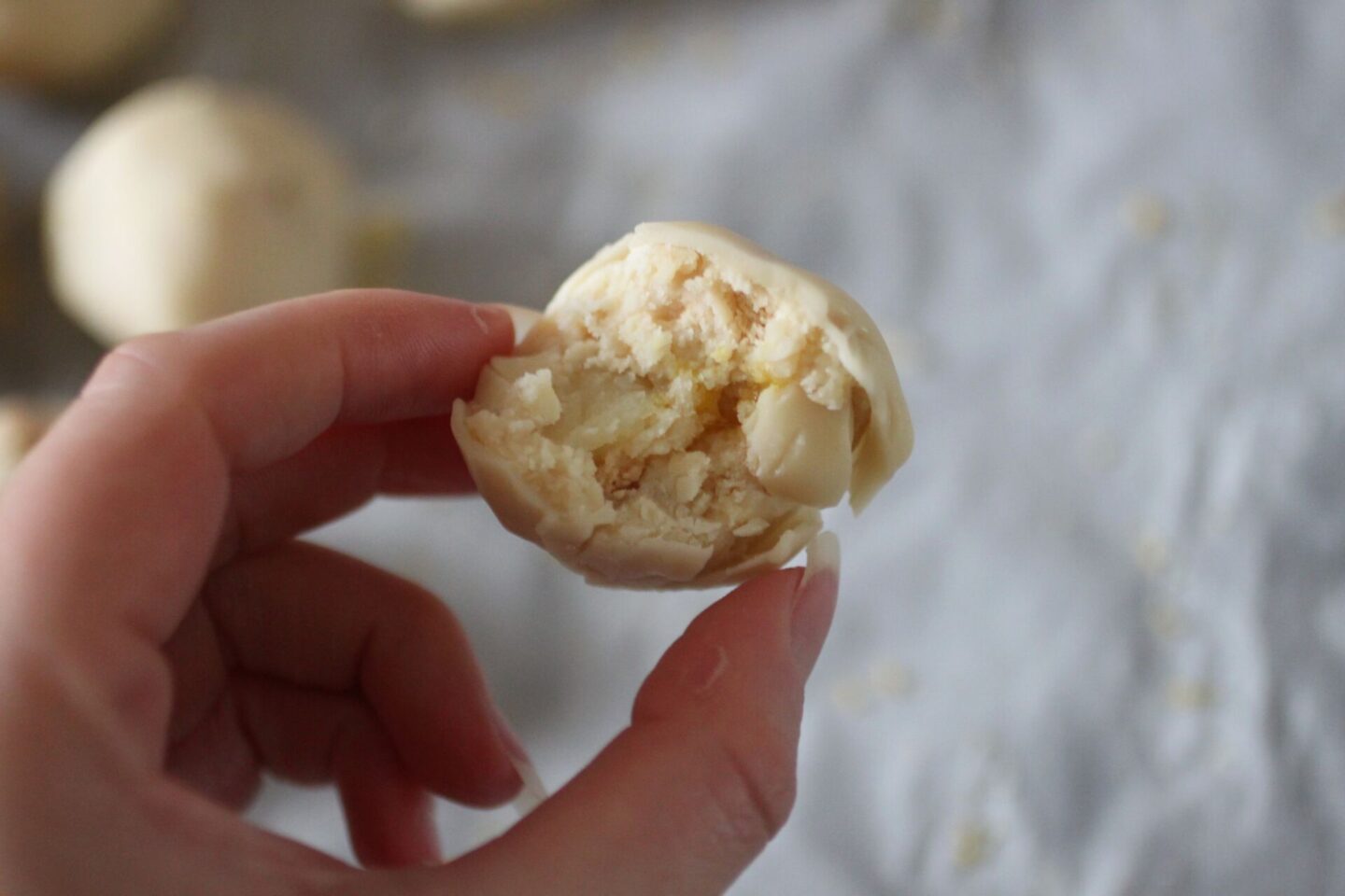 a hand holding up a lemon cheesecake ball to show texture