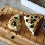 a slice of yoghurt toast on a wooden board with two small pots filled with blueberries and granola