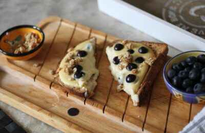 a slice of yoghurt toast on a wooden board with two small pots filled with blueberries and granola