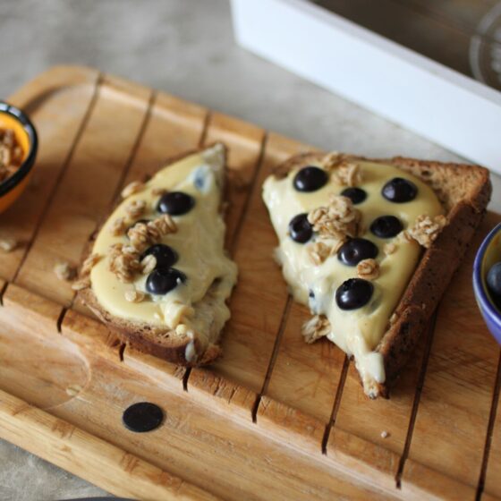 a slice of yoghurt toast on a wooden board with two small pots filled with blueberries and granola