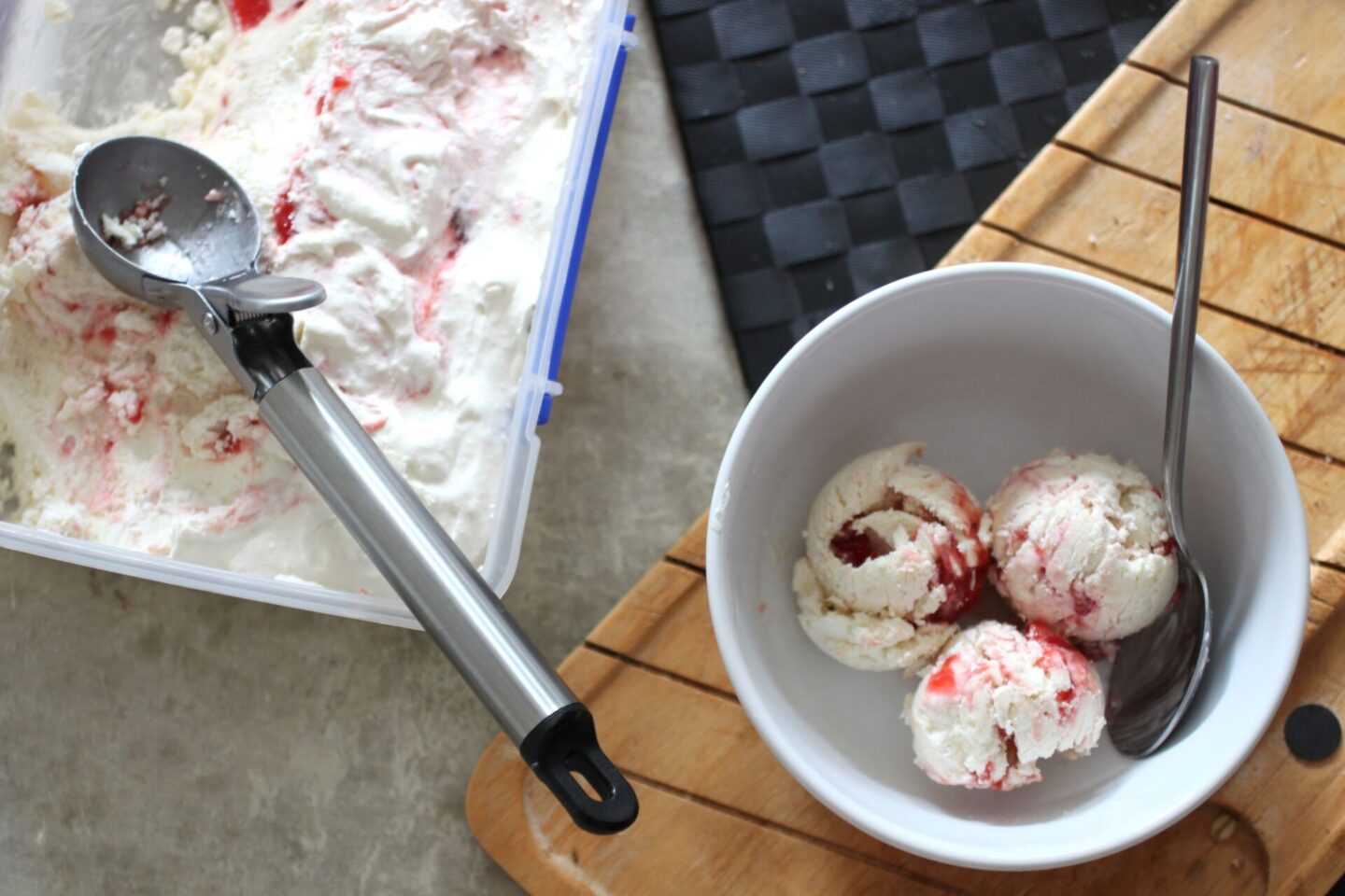 three scoops of firm scoop strawberry swirl ice cream in a white bowl next to container of ice cream