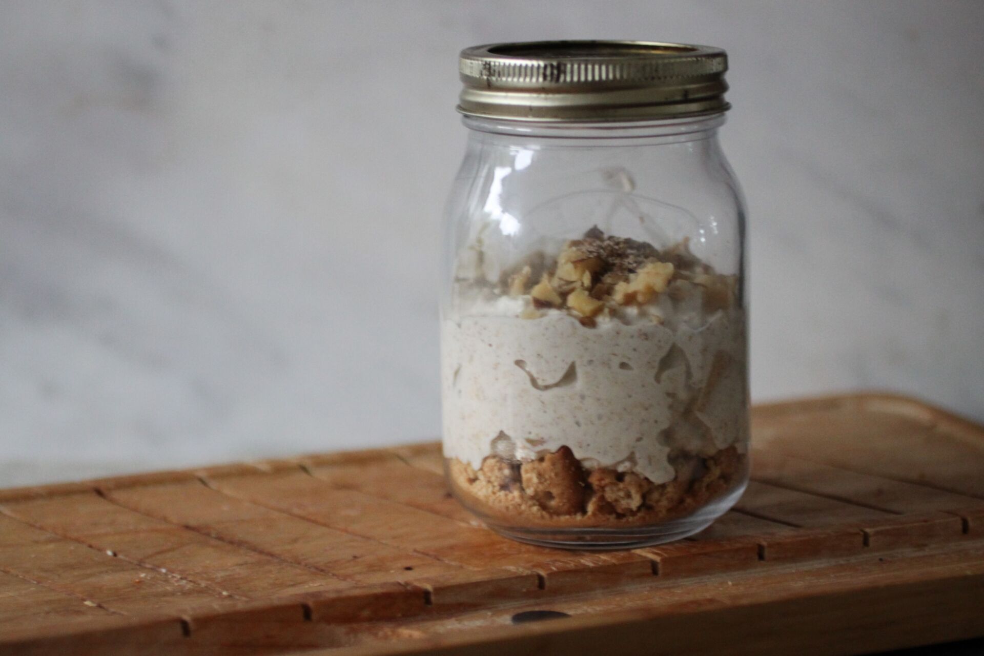 Mason jar of apple cheesecake overnight oats on a wooden board against grey backdrop